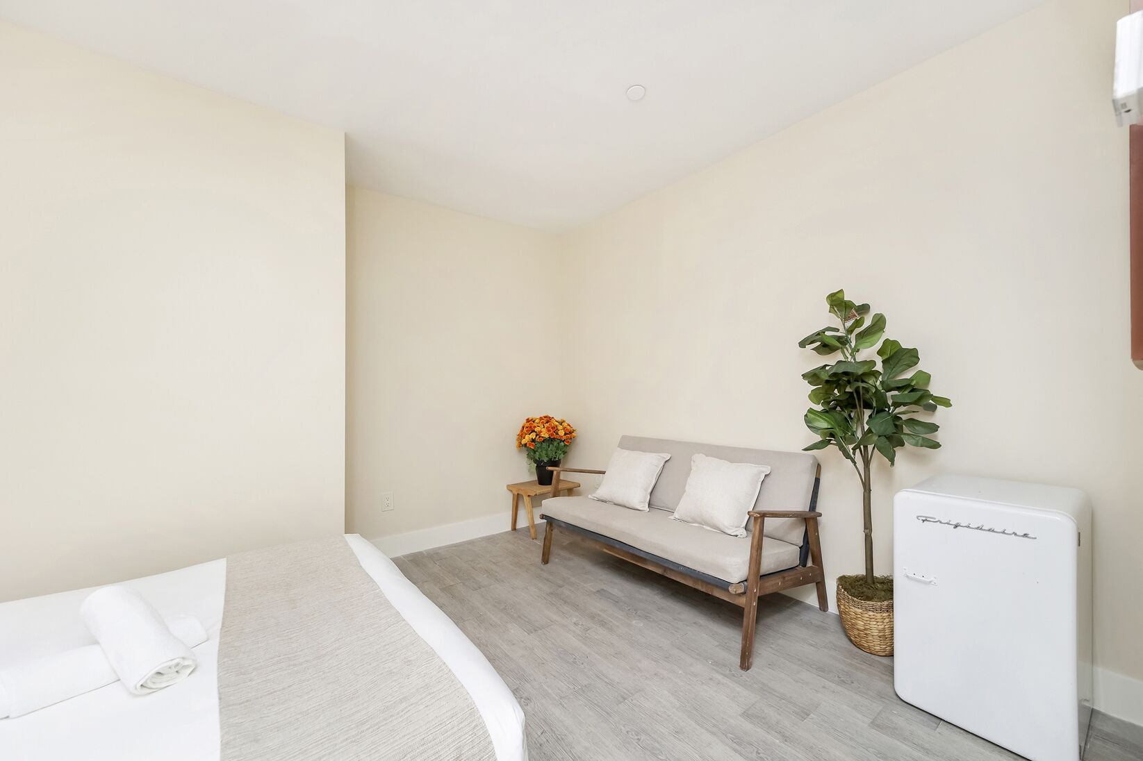 A bedroom with a bed, a sofa, a small table with a plant, and a white appliance.