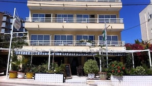 Un edificio de varios pisos con balcones, un letrero que dice "Hostal Roberto" y asientos exteriores con plantas en macetas.
