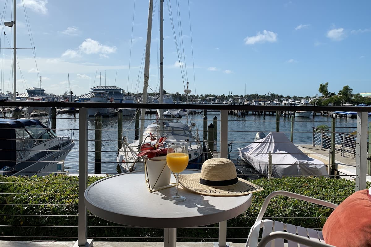 A table with a drink and a hat, overlooking a marina with boats.