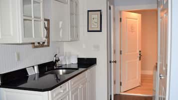 A kitchen with white cabinets, a black countertop, and a sink. There is a framed picture on the wall and a door leading to another room.