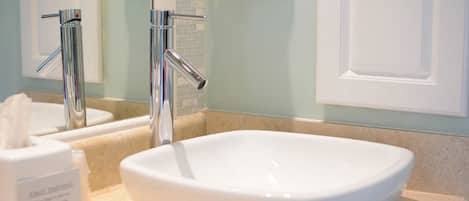 A bathroom with a white sink, chrome faucets, and a mirror reflecting a towel.