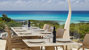 A dining table set for six with a clear view of the ocean and greenery in the background. - Hotel Maysi (Formentera)