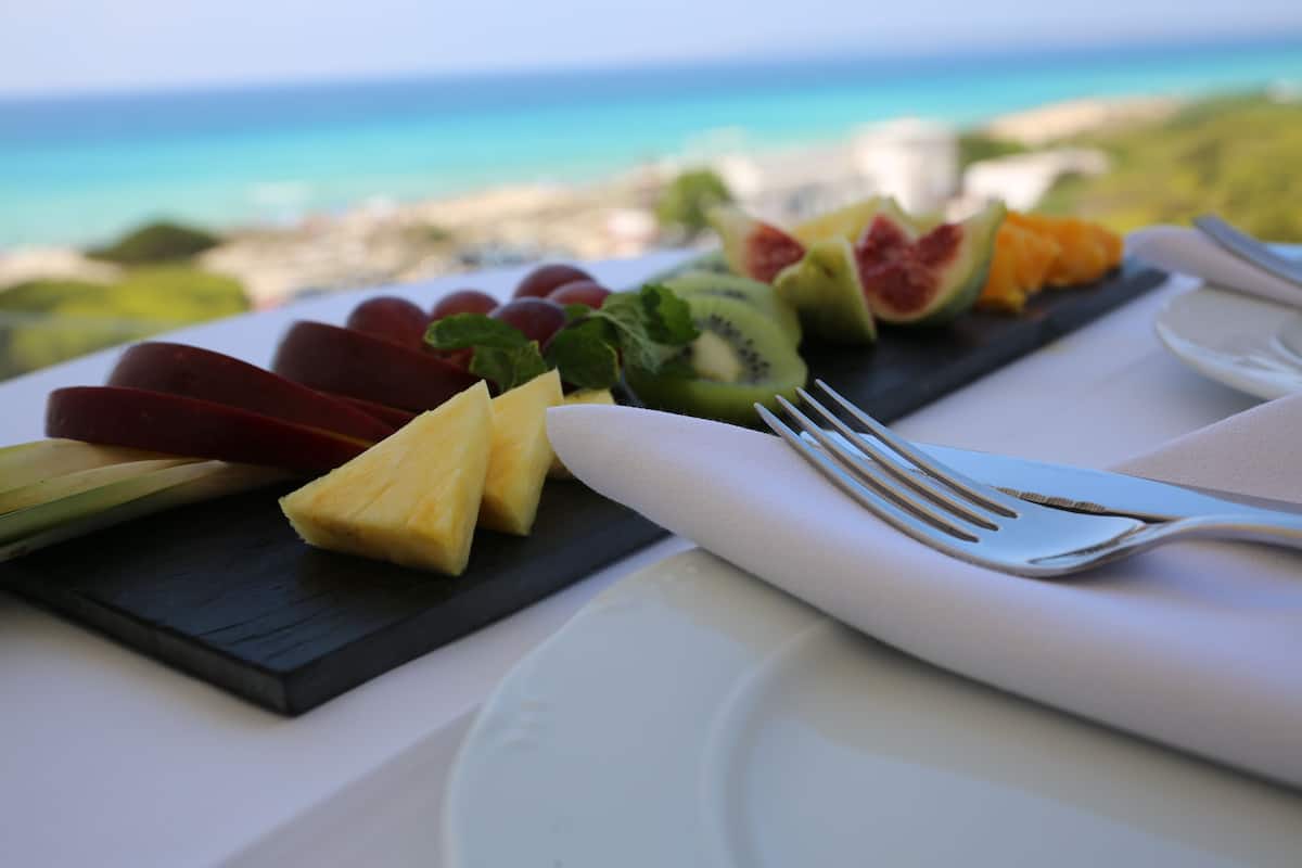 A fruit platter with a fork and napkin on a table with a view of the ocean.