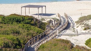 A wooden boardwalk leading to a beach with clear blue water and sandy shore. - Hotel Maysi (Formentera)