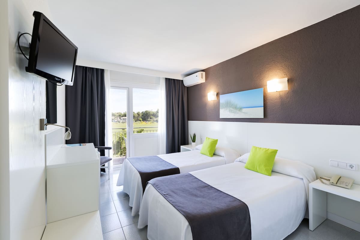 Ein Hotelzimmer mit zwei Betten, einem Fernseher, einem Telefon und Blick ins Freie.