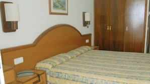A bedroom with a wooden bed frame, a patterned bedspread, a nightstand with a lamp, and a wardrobe. - Marina Playa de Palma (Playa de Palma)