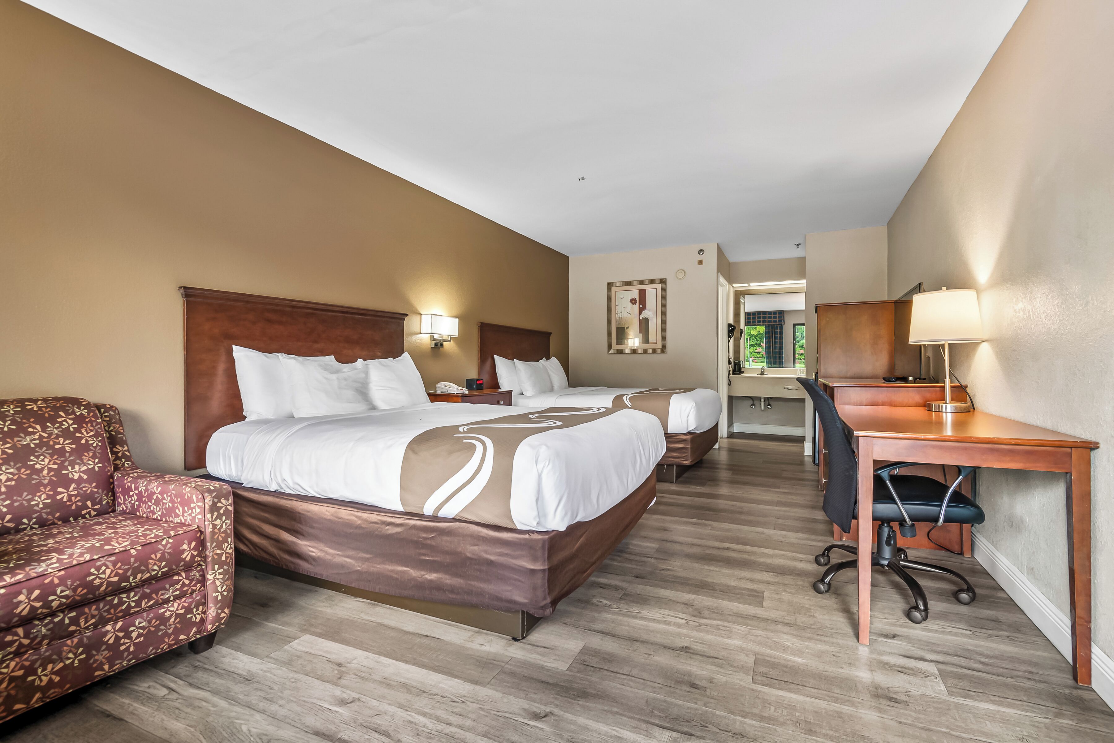 A hotel room with two beds, a desk, a chair, and a sofa.