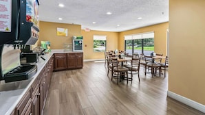 Una cocina moderna con cafetera, máquinas expendedoras y un comedor con mesas y sillas de madera.
