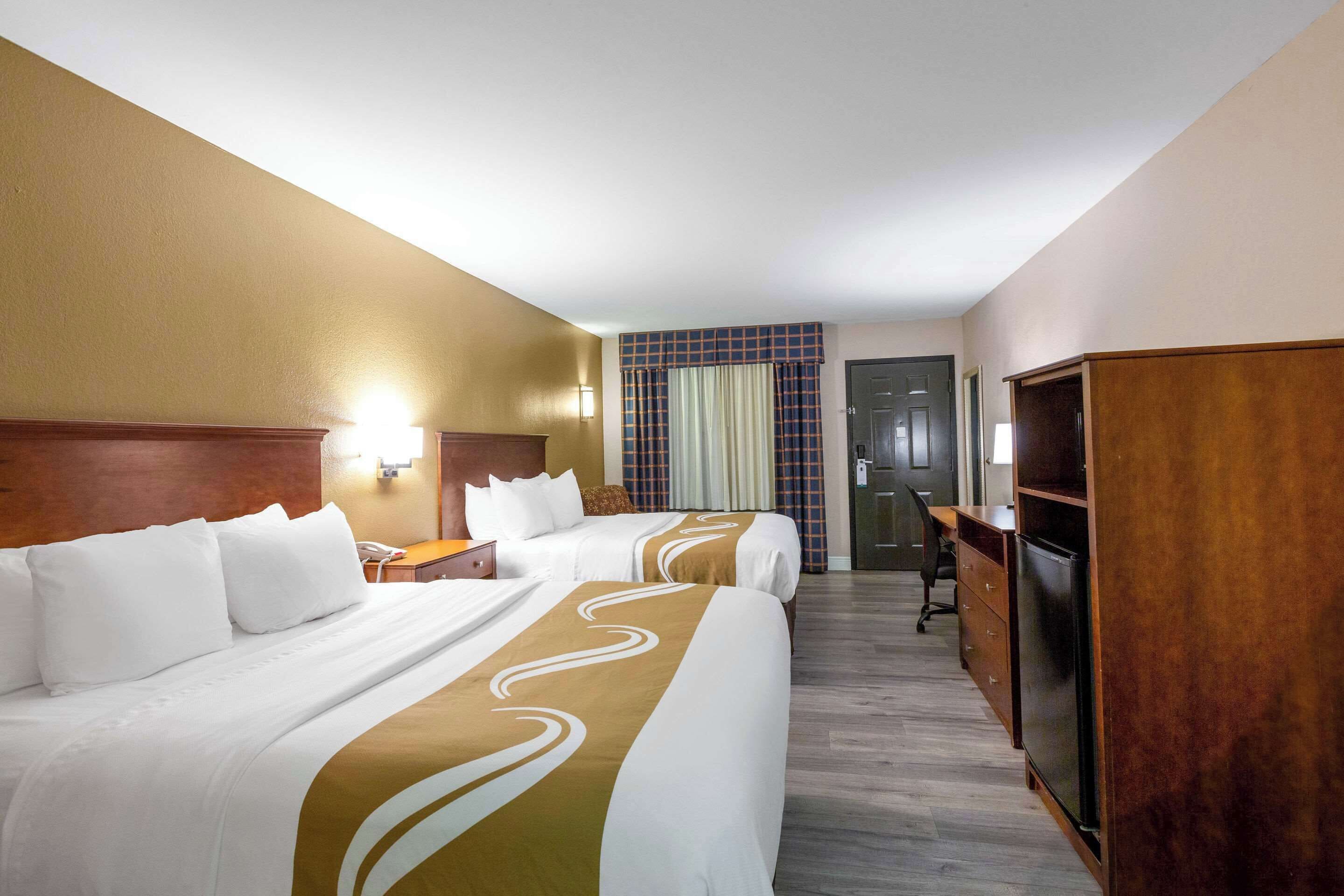 A hotel room with two beds, a desk, a chair, a wardrobe, and a door.