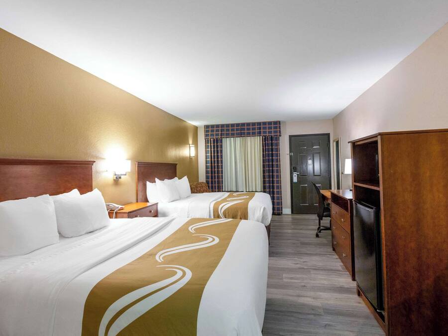A hotel room with two beds, a desk, a chair, a wardrobe, and a door.