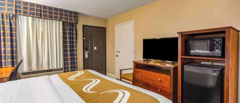 A hotel room with a bed, a television, a microwave, and a refrigerator.