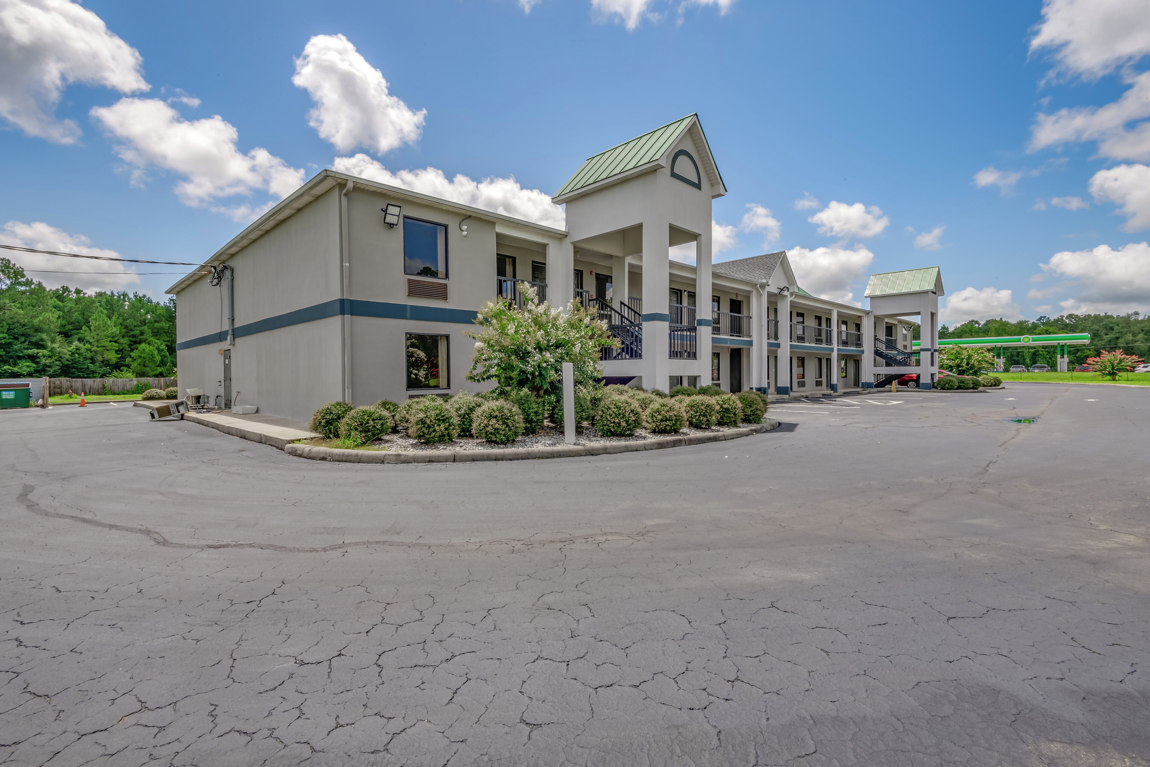 A two-story motel with a central tower, a parking lot, and a gas station in the background.