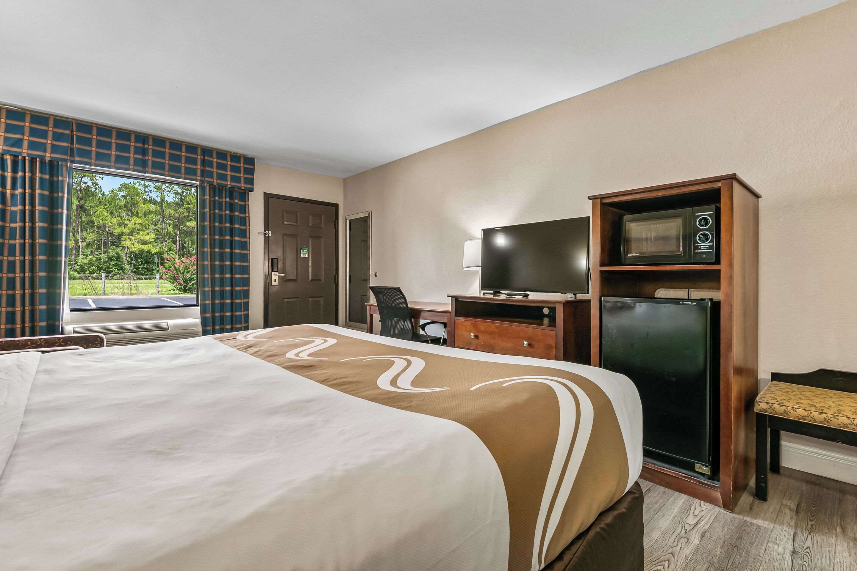 A hotel room with a large bed, a desk with a television, a microwave, and a view of the outdoors.