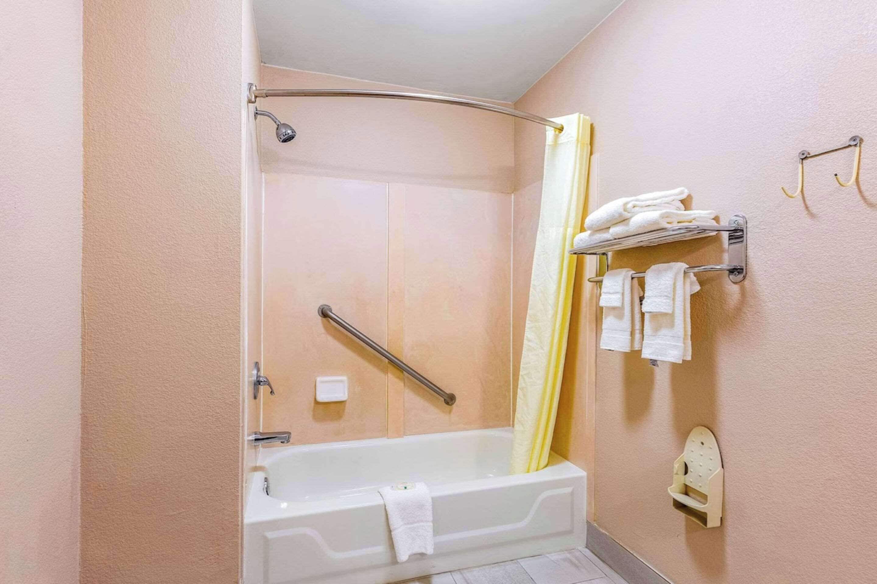 A bathroom with a bathtub, a shower, a handrail, a towel rack, and a toilet paper holder.