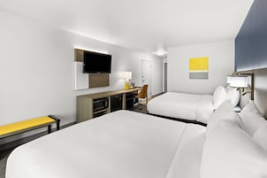 Habitación de hotel con dos camas, un escritorio, una silla, un televisor y una lámpara.