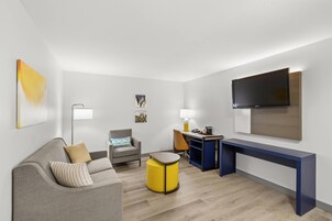 A modern living room with a sofa, armchair, small round table, desk, and a flat-screen TV mounted on the wall.