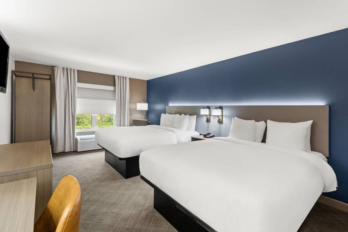 Quarto de hotel com duas camas, uma escrivaninha, uma cadeira, uma TV e uma janela com cortinas.
