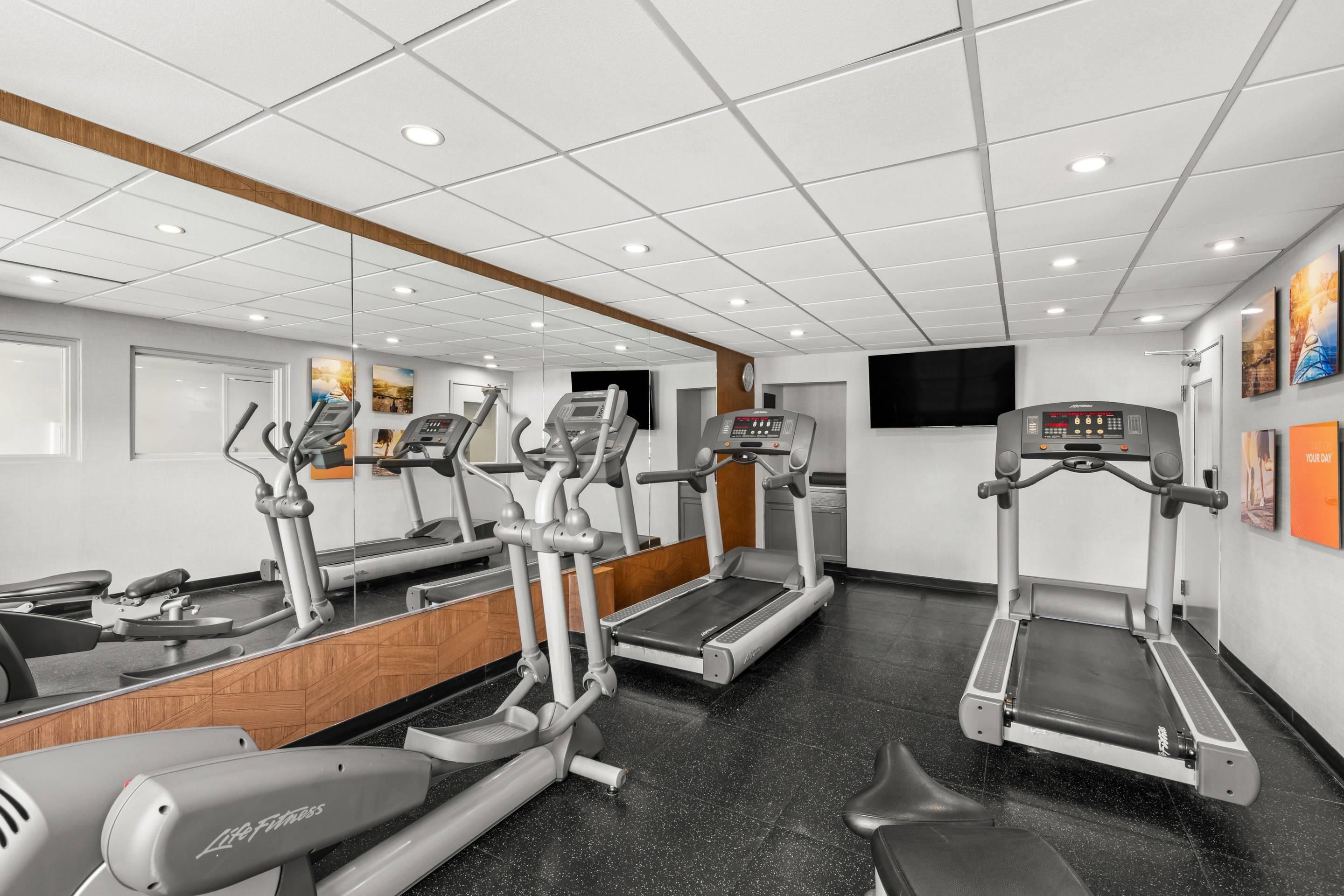 Une salle de sport équipée de tapis de course, de vélos elliptiques et d’un mur recouvert de miroirs.