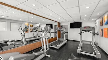 Une salle de sport équipée de tapis de course, de vélos elliptiques et d’un mur recouvert de miroirs.