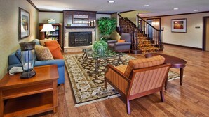 A spacious living area with a fireplace, a staircase, a sofa, a chair, and a coffee table. - Country Inn Suites By Radisson Rome Ga (Rome)