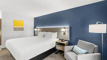 A hotel room with a bed, bedside table, lamp, and a chair.