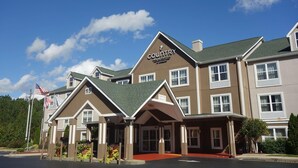A Country Inn & Suites with a traditional architectural style, featuring a prominent entrance with a covered porch, multiple windows, and a flagpole with an American flag. - Country Inn Suites By Radisson Rome Ga (Rome)