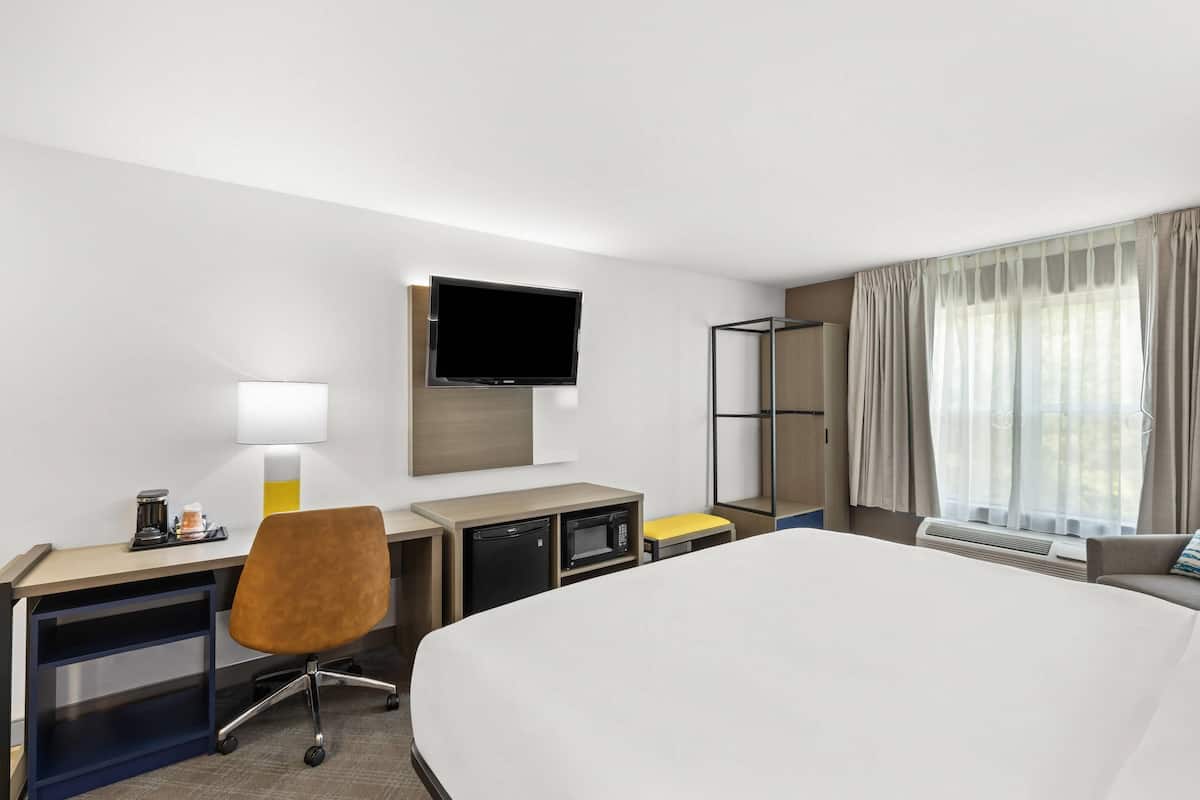 Quarto de hotel com cama, escrivaninha, cadeira, televisão e janela com cortinas.