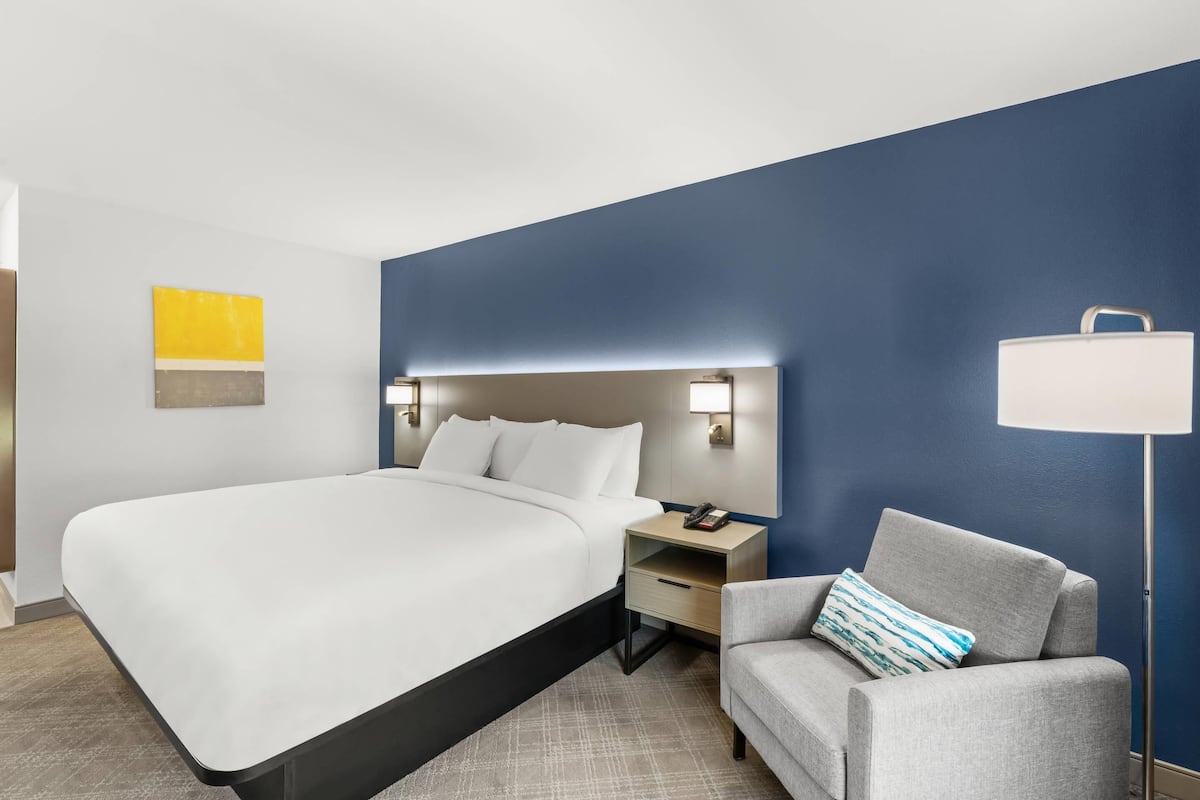 Quarto de hotel com cama, mesa de cabeceira, abajur e uma cadeira.