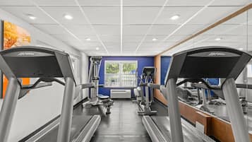 A gym with treadmills, weight machines, and a large window with a view of trees.