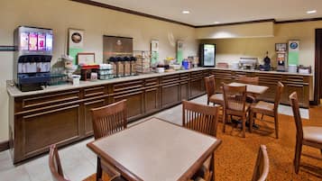 A hotel breakfast area with a self-service beverage station, a buffet bar, and seating arrangements.