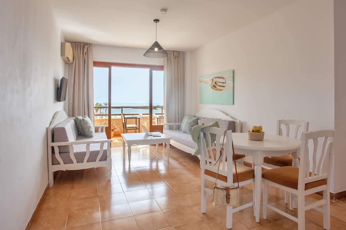 Een moderne woonkamer met een bank, een eettafel met stoelen, een balkon met uitzicht en een schilderij aan de muur.