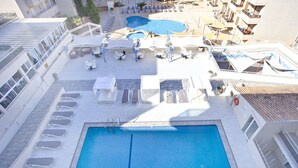 Vue aérienne d’un espace piscine sur le toit, avec plusieurs chaises longues, une petite piscine et une grande piscine centrale.