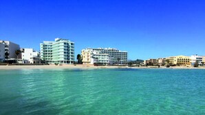 Un hôtel en bord de mer, avec plusieurs étages, une plage en arrière-plan et une eau d’un bleu limpide.