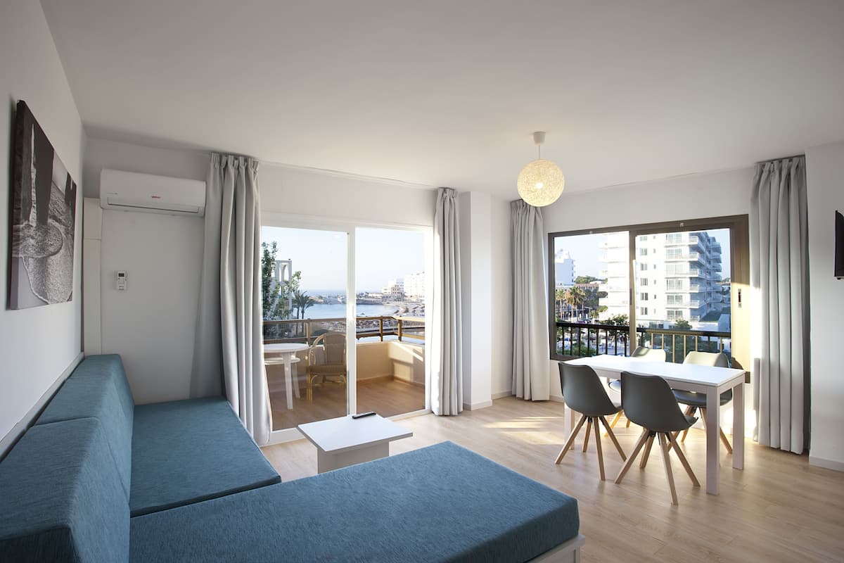Een moderne woonkamer met een bank, eettafel en stoelen, grote ramen met gordijnen en uitzicht op de stad.