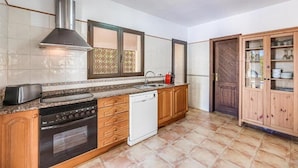 A kitchen with a stove, oven, dishwasher, and a cabinet with glass doors. - Villa Karen (Sa Rapita)