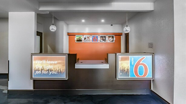 Et hotellets receptionsområde med et moderne design, inklusive en receptionsdisk, en digital informationsskærm og flere indrammede billeder på væggen.