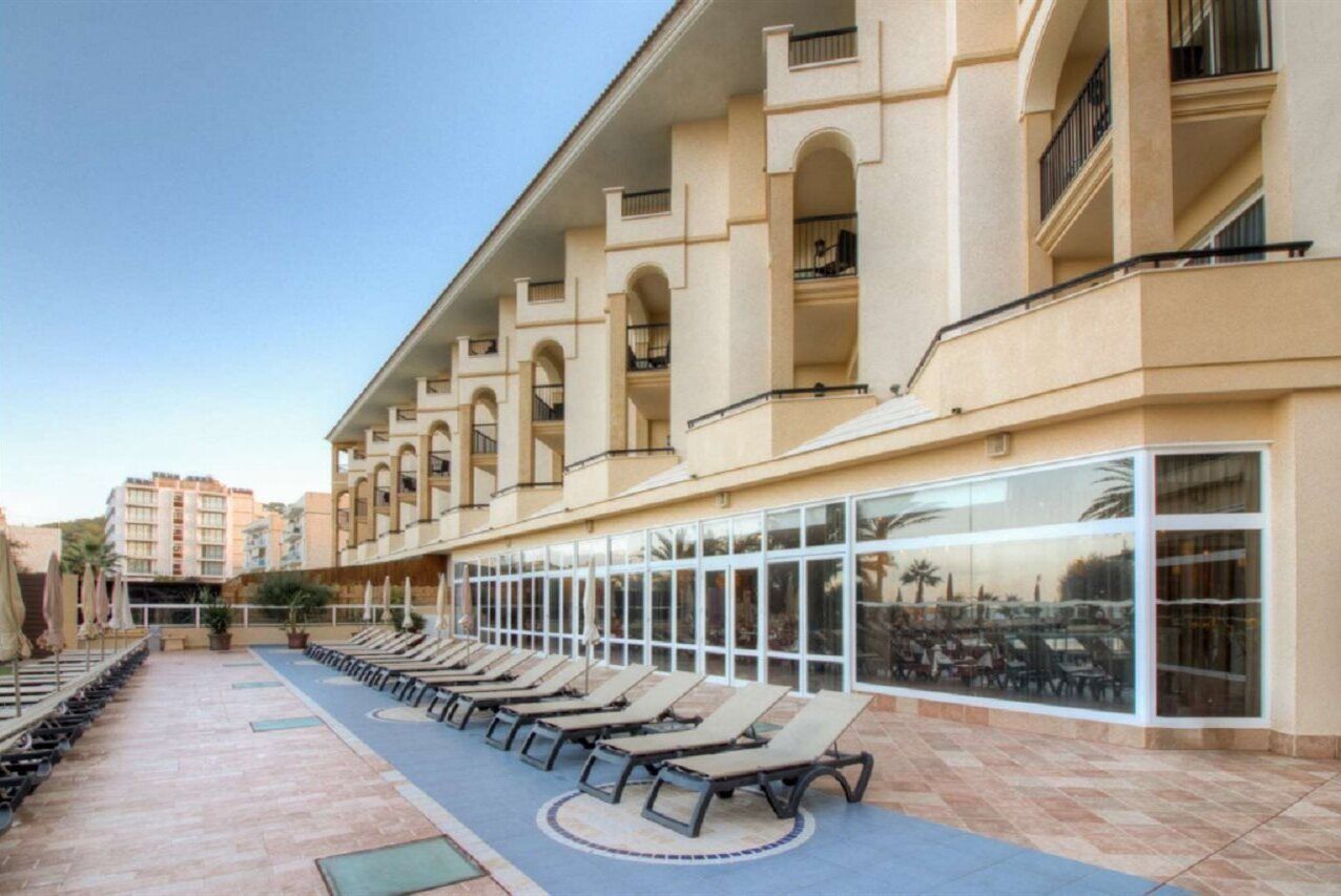 Ein Hotel mit Poolbereich, der Liegestühle und eine überdachte Lounge mit Tischen und Sonnenschirmen bietet.