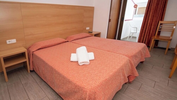 Een hotelkamer met twee bedden, een houten hoofdbord, een tafeltje en een stoel.