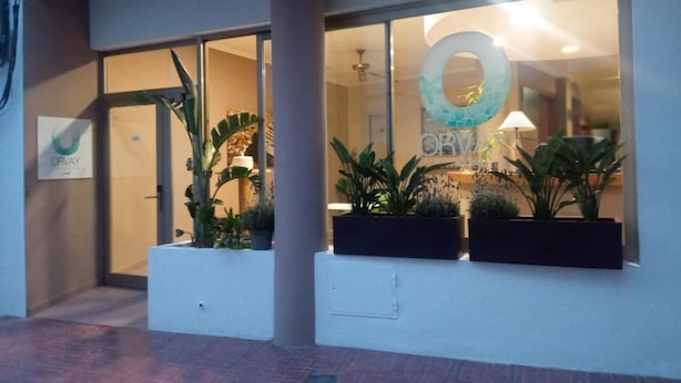 A hotel entrance with a large glass window, a sign reading "ORVAY", and potted plants in front. - Orvay Apartments (Sant Antoni de Portmany)
