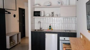 A compact kitchen with a microwave, sink, and small refrigerator. There is a wooden table and a bench in the foreground. - Orvay Apartments (Sant Antoni de Portmany)