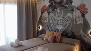 A double bed with two towels, a patterned wall mural, and a small stool. - Orvay Apartments (Sant Antoni de Portmany)