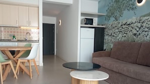 A modern kitchen with a dining area, a living room with a sofa, and a small table with chairs. - Orvay Apartments (Sant Antoni de Portmany)