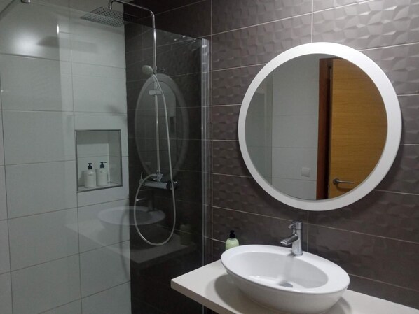 A modern bathroom with a glass-enclosed shower, a round mirror, and a white sink.