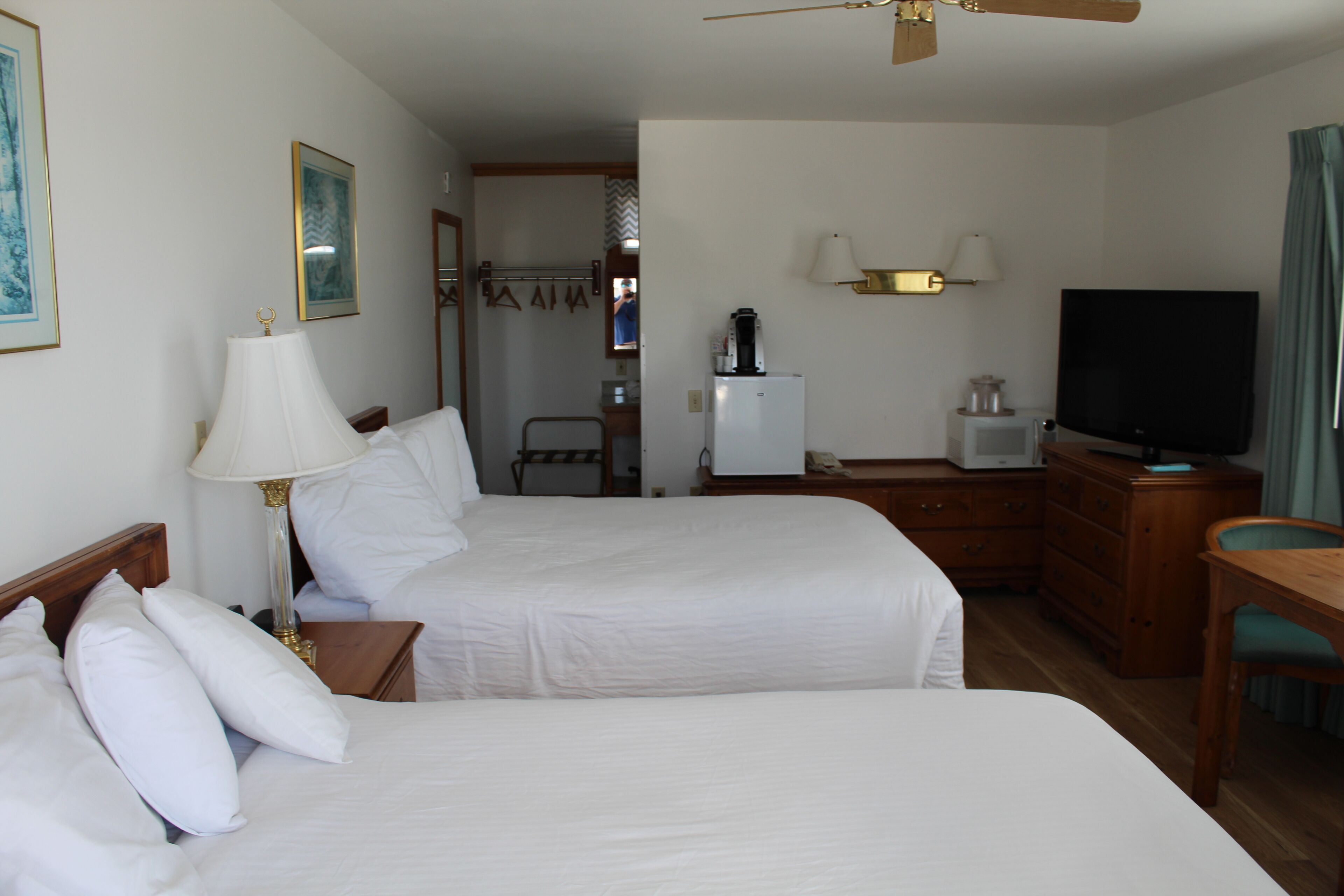 Habitación de hotel con dos camas, un escritorio, un televisor, un refrigerador y una lámpara.