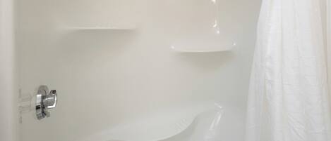 A bathroom with a white shower, a glass shower door, and a white bathtub.