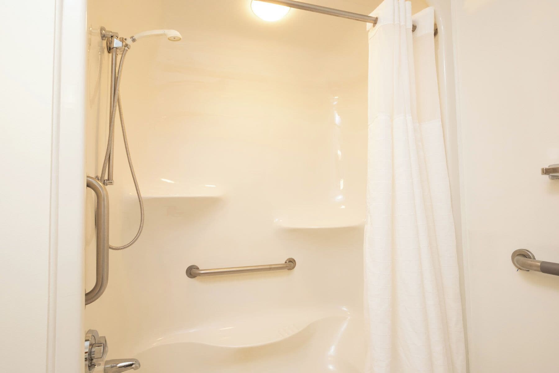 A bathroom with a shower, a handrail, and a towel rack.