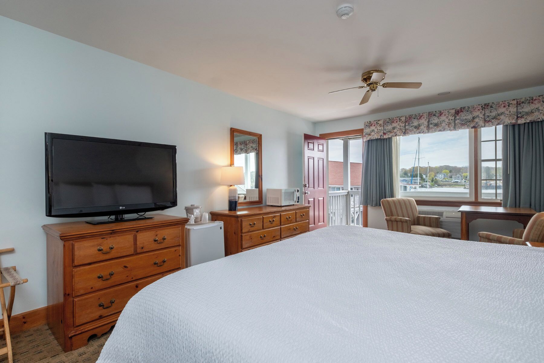 A hotel room with a bed, a television, a dresser, a desk, and a view of the outside.