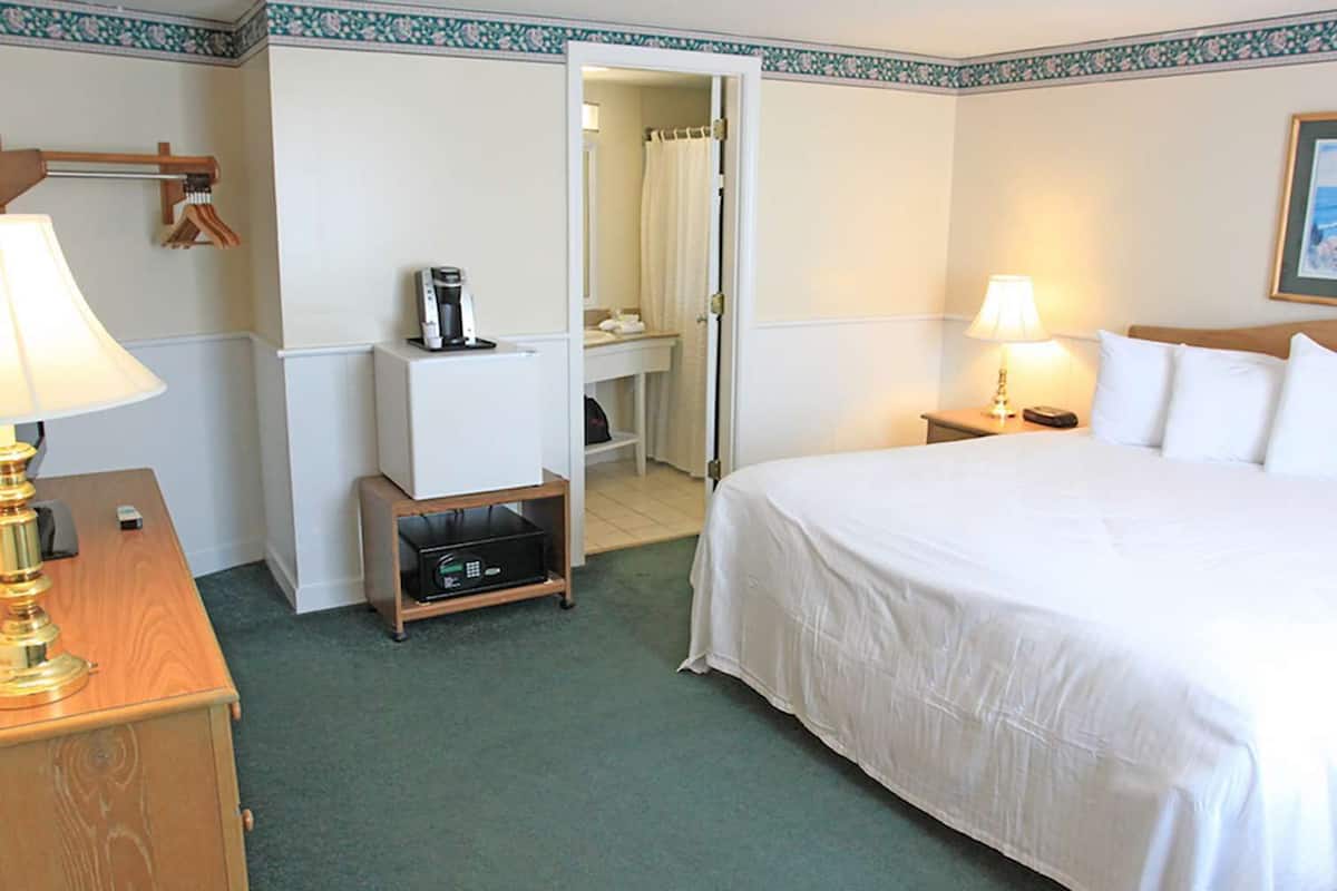 A hotel room with a bed, bedside lamps, a desk with a lamp, a coffee maker, and a small cabinet.
