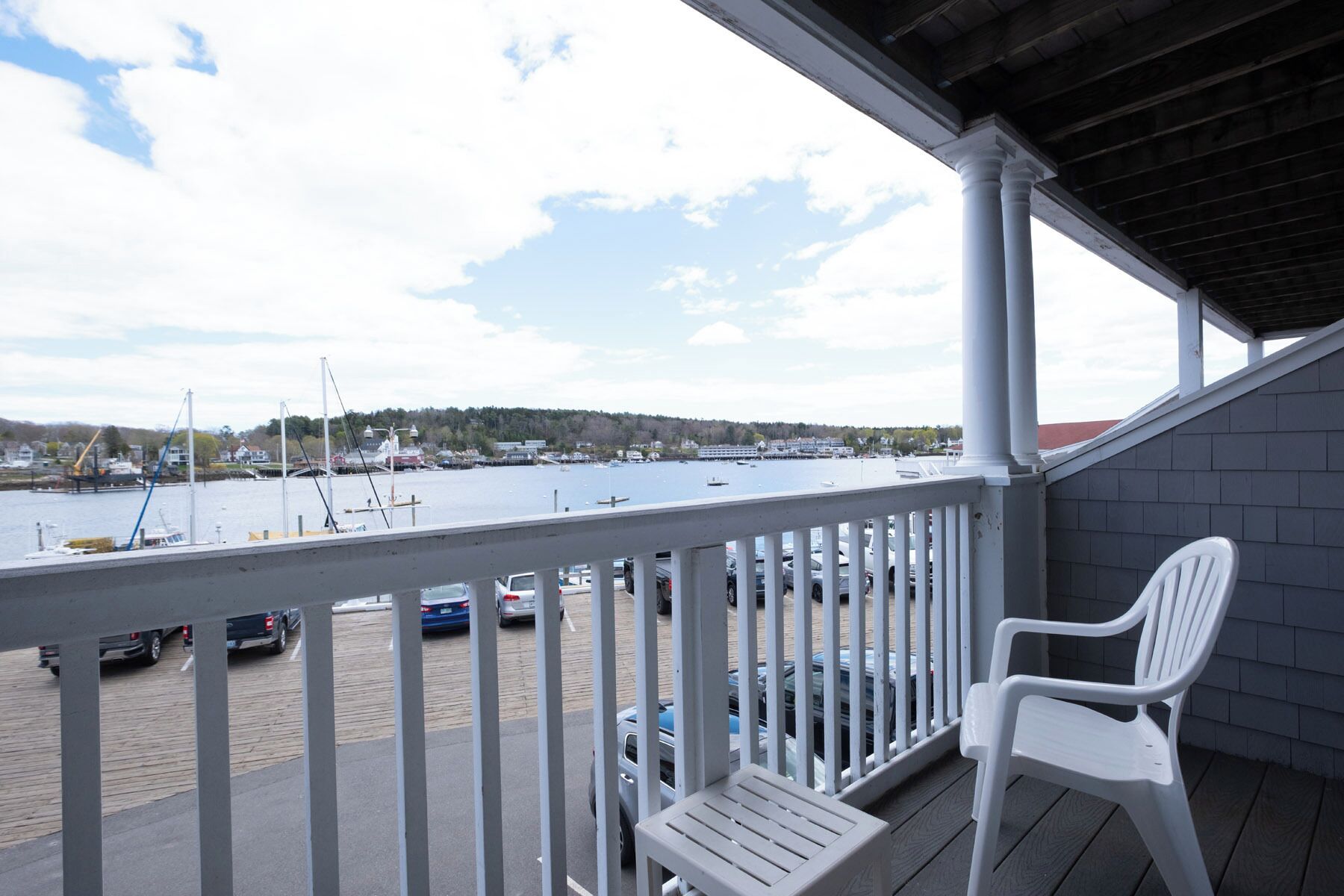 Een balkon met uitzicht op een jachthaven, een witte kunststof stoel en een gebouw met een donker dak.