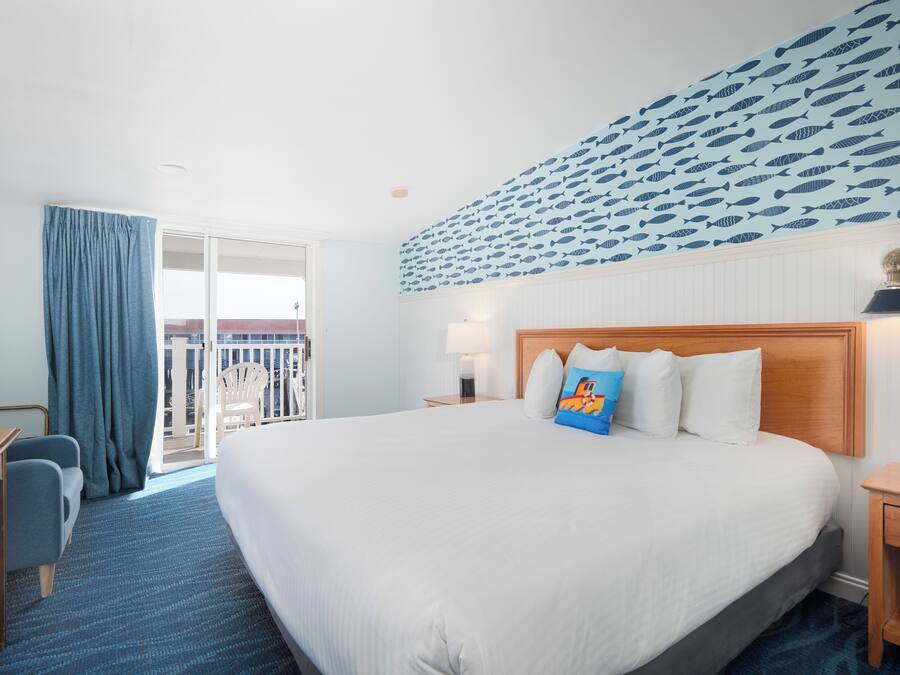 A hotel room with a large bed, a desk, a chair, and a balcony with a view.